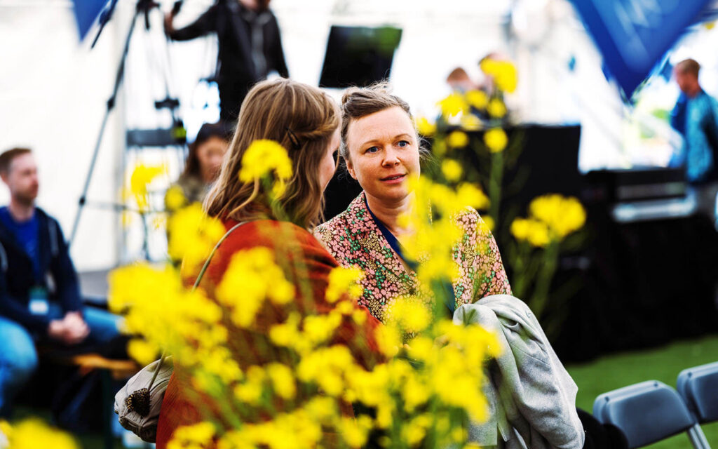 Besökare på Next is Now Matfestival. Gula blommor i förgrunden.