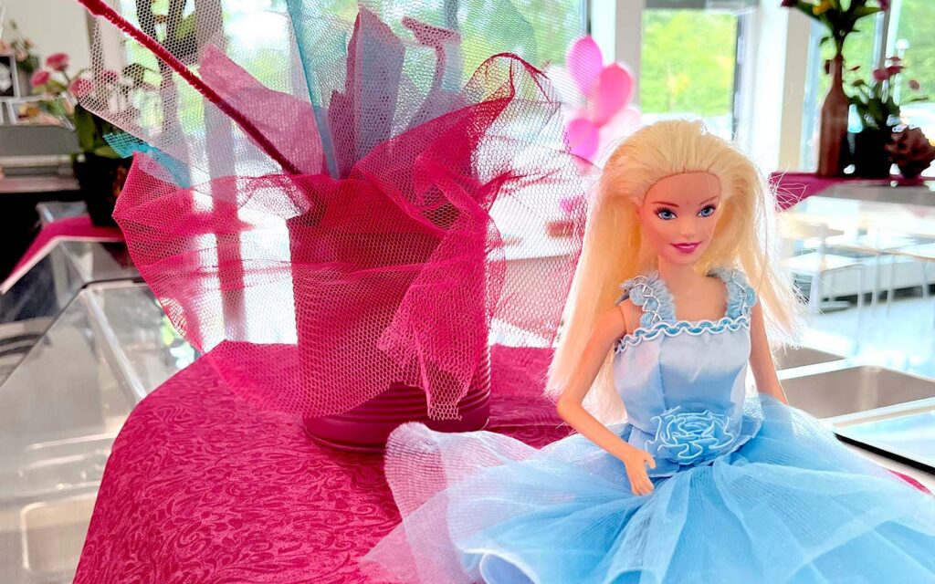 Barbie-docka i blå klänning sitter framför rosa tyll-dekoration.