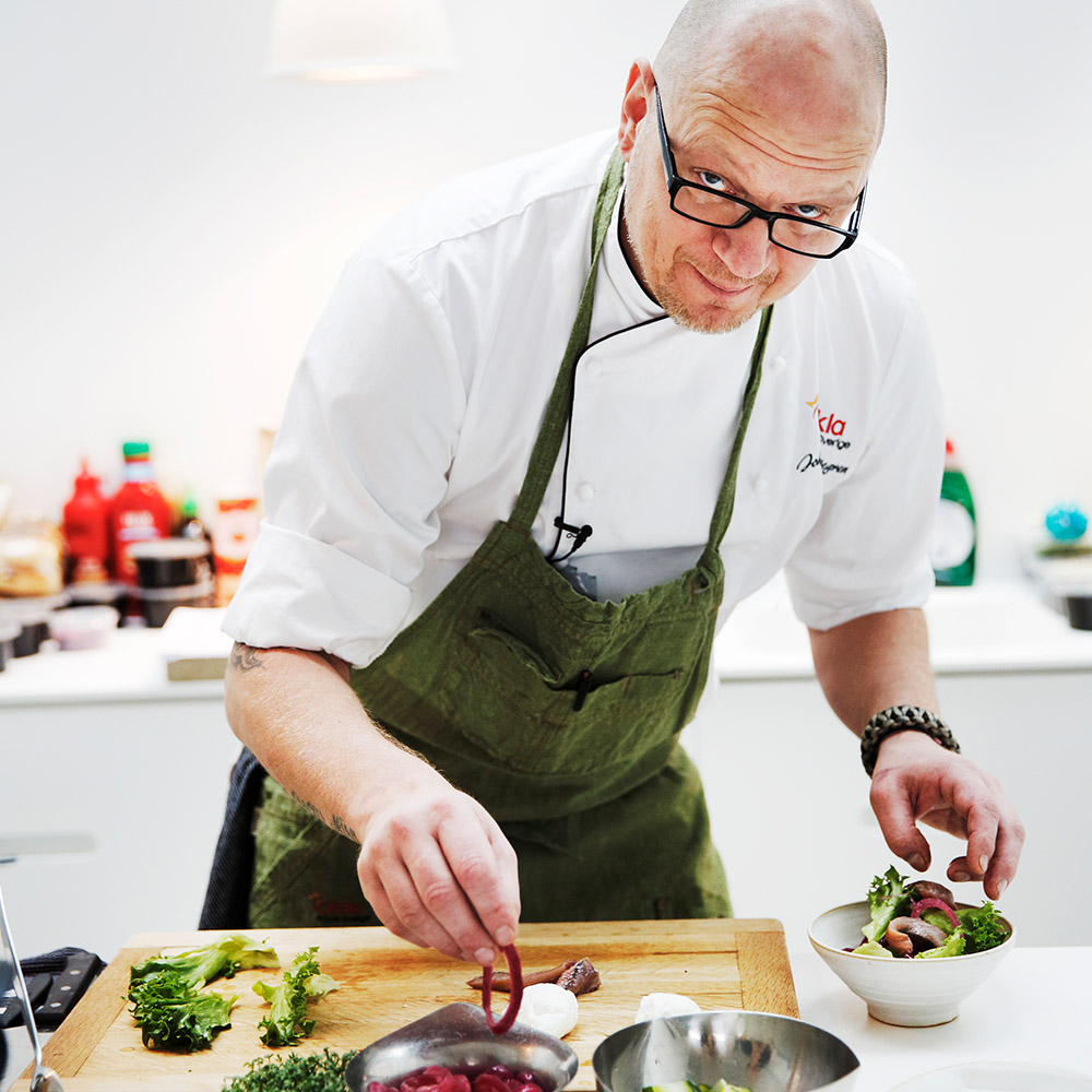 Kock står vid köksbänk och fixar med en sallad som läggs upp i en skål.