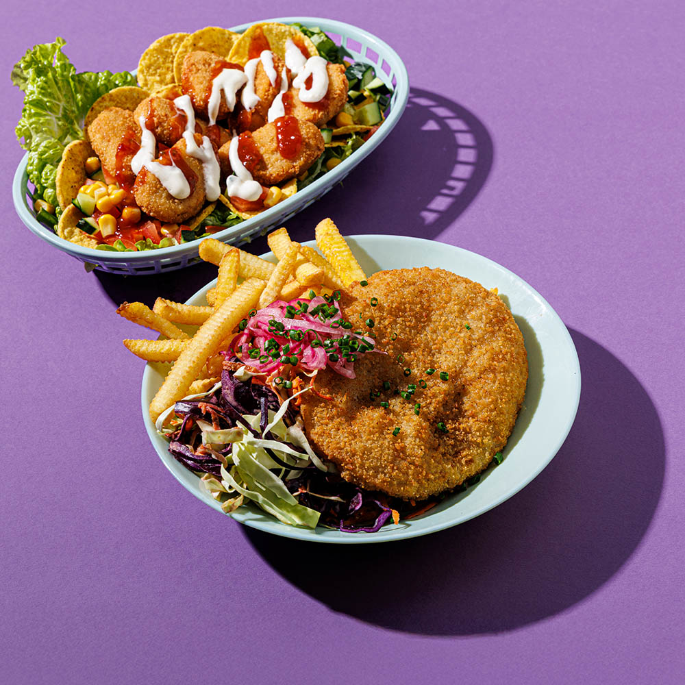 Tallrikar med schnitzel och nugget serverade mot lila bakbrund.